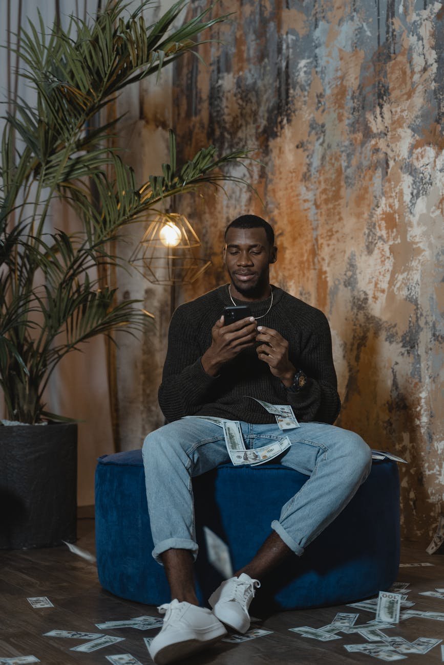 a man in black long sleeves sitting on blue sofa chair while using his phone